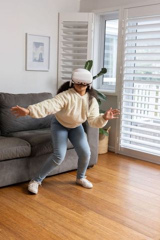 Young girl wearing vr headset playing and exploring virtual world in modern living room