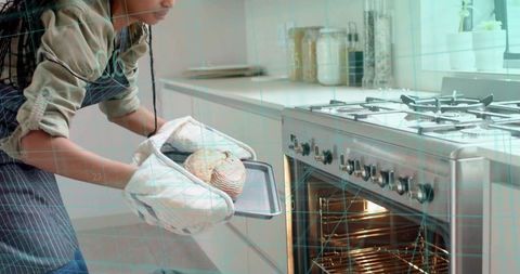 Home baker removing golden rolls from stainless steel oven wearing striped apron and mitts