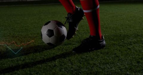 Soccer player juggling ball on night turf wearing red socks and black cleats