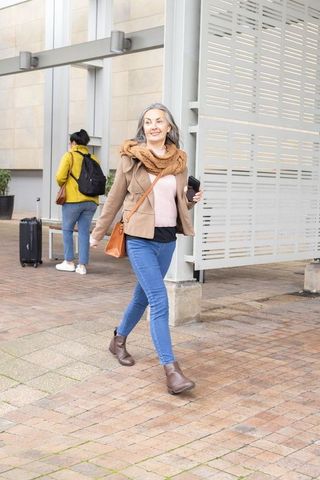 Mature woman walking confidently through transit concourse wearing scarf and crossbody bag