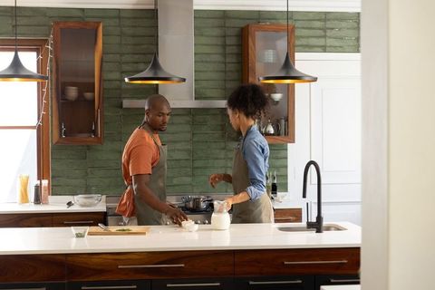Couple cooking together at kitchen island, preparing meal with pots and cutting board