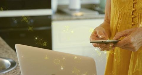 Senior man tapping smartphone and laptop on granite kitchen counter with yellow overlay