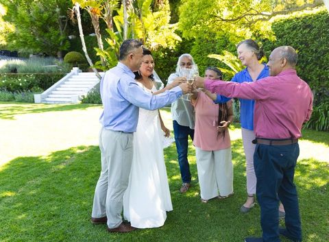 Bride raising flute with family toasting in sunlit garden, animated bubbles, outdoor wedding