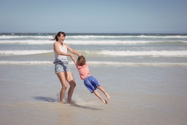 Happy mother enjoying with son on shore at beach during sunny day