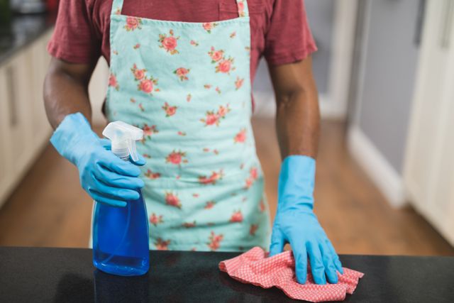 Mid section of man holding spray bottle and rag in kitchen at home