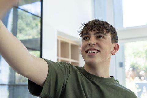 Teenage boy smiling reaching in bright modern home interior wearing olive t-shirt