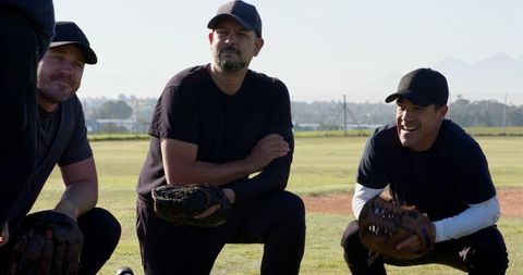 Kneeling adult baseball players holding leather gloves and smiling during outdoor practice