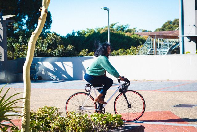 Mid adult African American businesswoman riding a bicycle in an urban area. Ideal for illustrating eco-friendly commuting, sustainable transportation, and healthy lifestyle choices. Suitable for use in articles, advertisements, and campaigns promoting green living, urban mobility, and professional life balance.