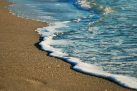 Gentle Foam Washing Over Golden Sand Shoreline with Clear Turquoise Water Close-Up
