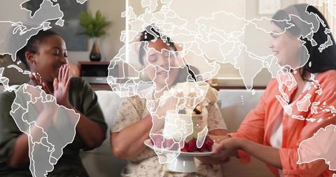Friends celebrating birthday presenting berry cake with candle on cozy sofa, world map overlay