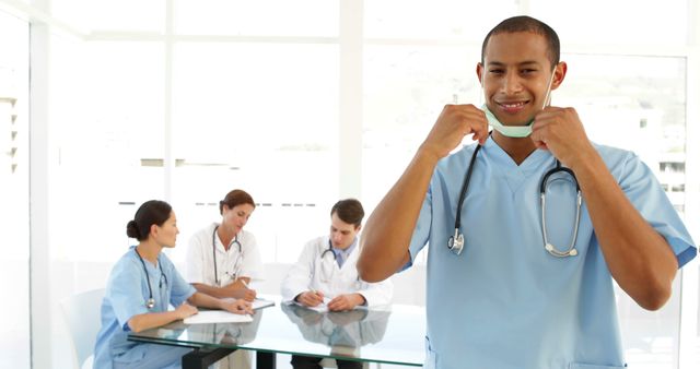 Male Nurse Preparing for Work while Colleagues Collaborating in Background - Download Free Stock Photos Pikwizard.com