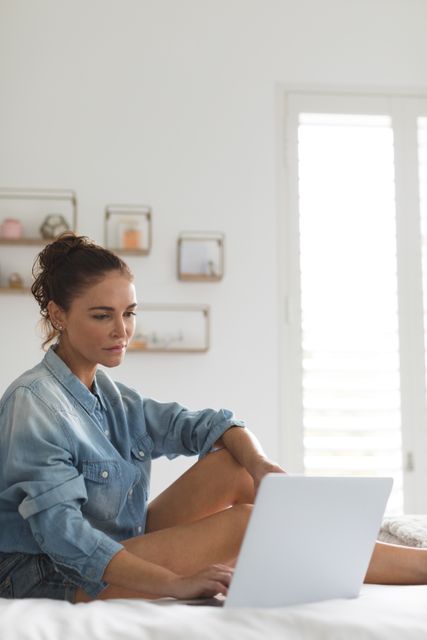 Beautiful woman using laptop on bed in bedroom at comfortable home
