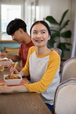 Smiling asian couple enjoying noodle meal at home dining table