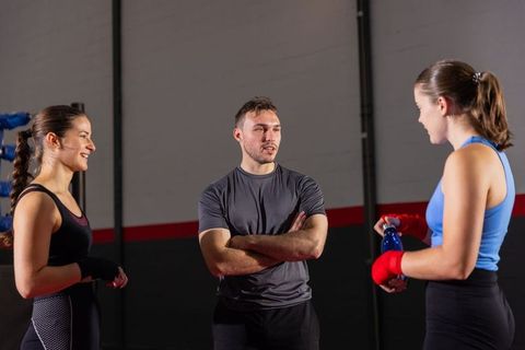 Boxing trainer instructing two female boxers in ring corner during gym training