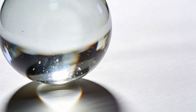 Clear crystal sphere casting caustic light and reflections on minimal white surface