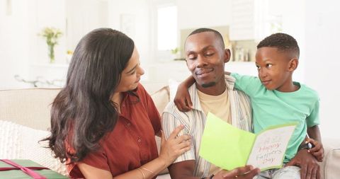 Father receiving handmade father's day card while family celebrating together on cozy sofa