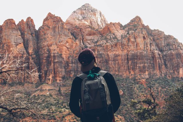 A person wearing a backpack is hiking and looking at a mountain range, showcasing a love for travel and outdoor adventures. The impressive cliffs and natural terrain are perfect for promotional use in travel blogs and outdoor gear advertisements. Ideal for inspiring wanderlust and an adventurous spirit.