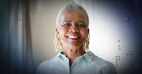 Smiling mature woman wearing hoop earrings and floral shirt in softly lit interior