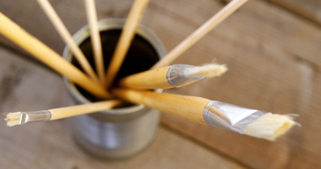 A collection of paintbrushes with wooden handles and various bristle sizes are stored bristles-up in a container. These tools are essential for artists and painters to create their work, showcasing the diversity of brush types used in the creative process.