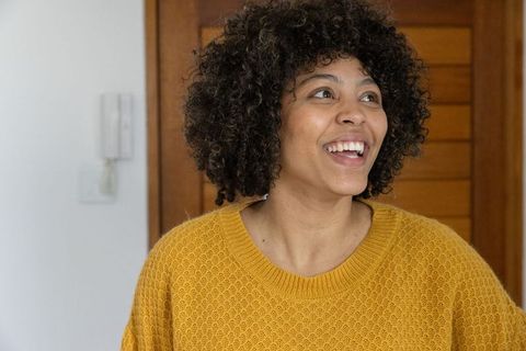 Smiling african american woman in mustard sweater looking up in warm home entryway