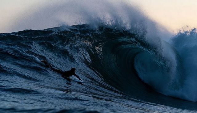 Lone surfer paddling into towering barrel wave at dawn reef break