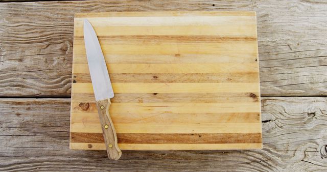 A kitchen knife rests on a well-used wooden cutting board, with copy space. The arrangement suggests preparation for cooking or the completion of a food preparation task.