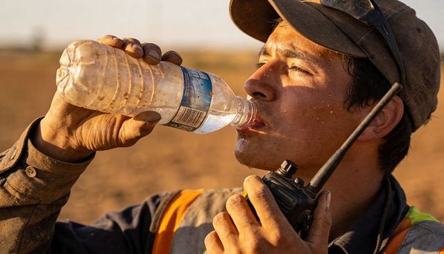 Field laborer drinking water while holding walkie-talkie during hot summer outdoor workday