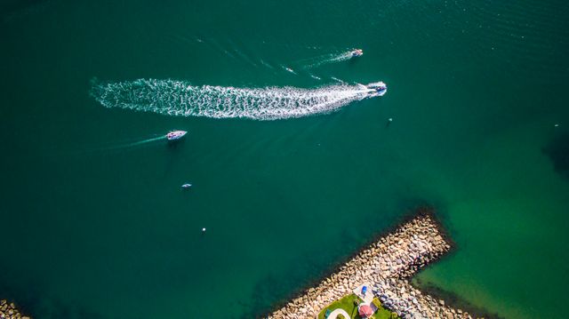 Aerial perspective showcasing boats speeding across clear blue waters near a rocky coastline. Ideal for use in travel promotions, articles on marine activities, and outdoor lifestyle content.
