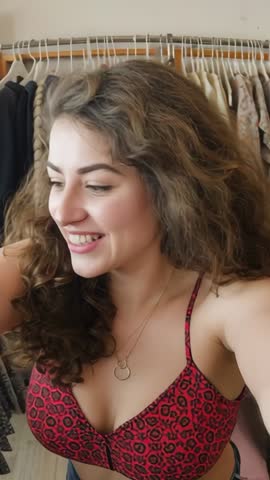 Vertical lifestyle video woman browsing closet, trying on red patterned spaghetti top, smiling