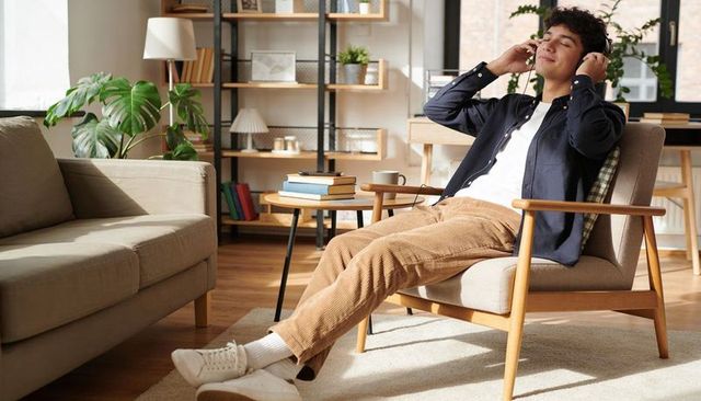 Young man relaxing with headphones in sunlit midcentury living room, cozy home interior