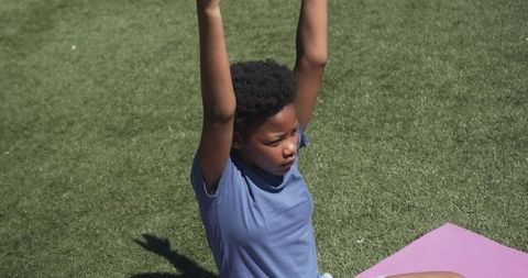 Young female stretching arms overhead on pink mat in park practicing outdoor yoga
