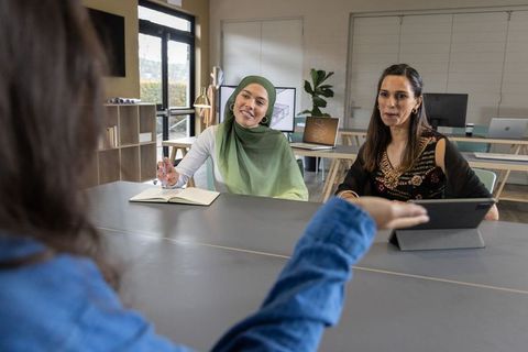 Multicultural female team collaborating in modern office with hijab woman taking notes