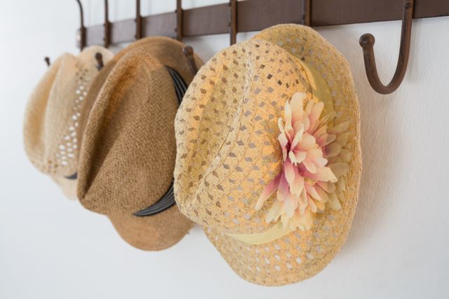 Close-up view of straw hats hanging on wall hooks against a white wall. Ideal for use in articles or advertisements related to fashion, summer accessories, home decor, and organization tips.