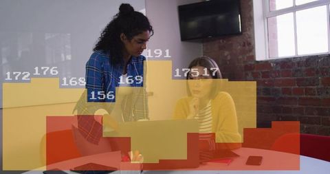 Two women collaborating over laptop while analyzing marketing data overlays and metrics