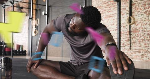 Stretching male athlete reaching toward foot after intense workout in industrial gym rig