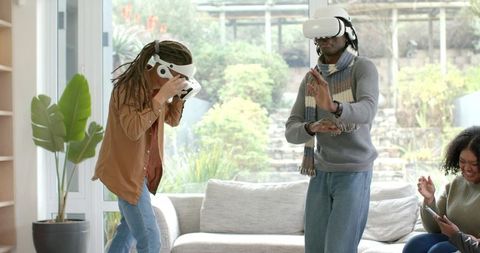 Diverse friends playing VR games in bright modern living room with gray sofa