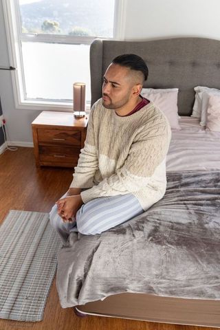 Contemplative man sitting on bed wearing sweater and striped pajamas in cozy bedroom light