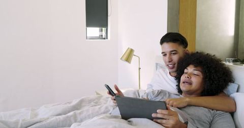 Happy Couple Relaxing in Bed Sharing Digital Devices