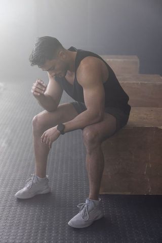 Focused athlete resting on plyometric box after intense training, wearing fitness tracker