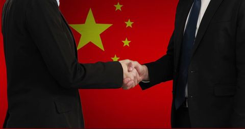 Businessmen in suits shaking hands over chinese flag