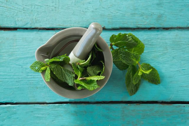 Overhead view of mint leaves with mortar and pestle on wooden table