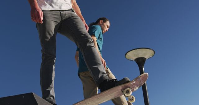 Two skateboarders stand on top of a skate ramp under a clear blue sky ready to drop in. They are dressed in casual clothing, and the clear weather enhances the scene. Ideal for use in articles about extreme sports, youth culture, and outdoor activities.
