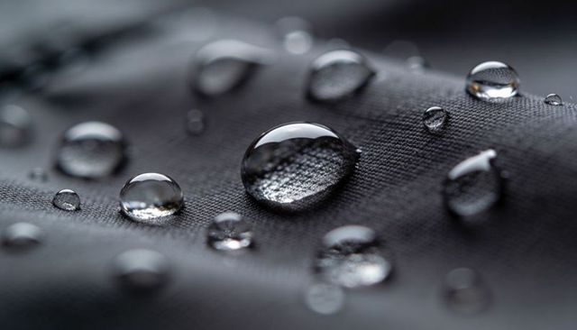 Macro water beads on dark woven fabric showcasing waterproof textile technology and texture