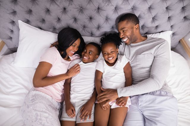 Happy African American family lying on bed, smiling and bonding. Perfect for themes of family togetherness, love, and home life. Ideal for advertisements, family-oriented articles, and lifestyle blogs.