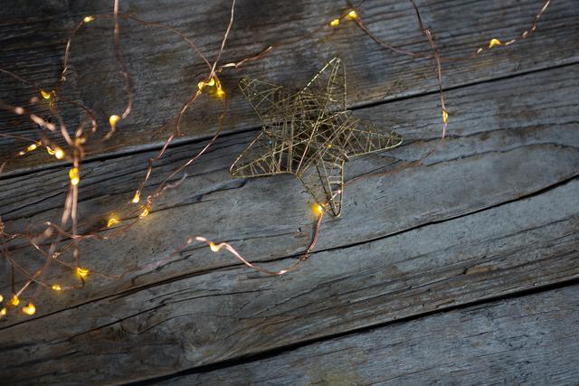 This image features a Christmas star and fairy lights on a rustic wooden plank, creating a warm and festive atmosphere. Ideal for holiday greeting cards, seasonal advertisements, social media posts, and Christmas-themed blog content. The warm glow and rustic background evoke a cozy and inviting holiday spirit.