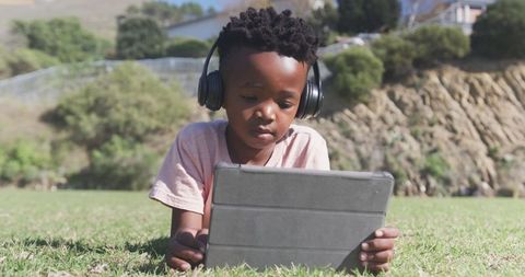 Boy with Headphones Using Tablet Outdoors In Park