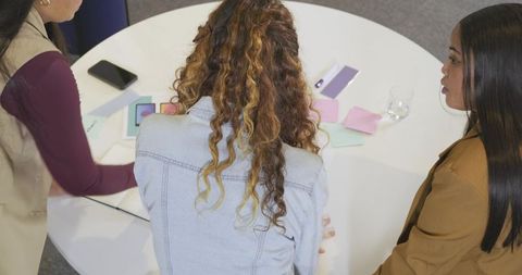 Diverse women collaborating around round table reviewing color swatches and mobile phones