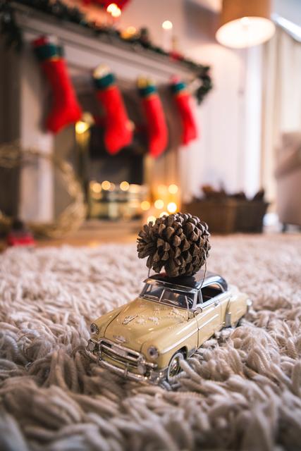 Vintage toy car carrying a pine cone on a cozy rug in a festive living room. Fireplace with stockings and holiday decorations in the background. Ideal for holiday greeting cards, festive advertisements, and home decor inspiration.