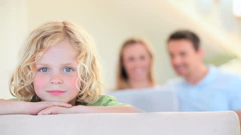 Child Relaxing on Sofa with Happy Parents in Distance