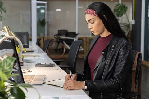 Focused professional writing in notebook at modern coworking desk with laptop and bike